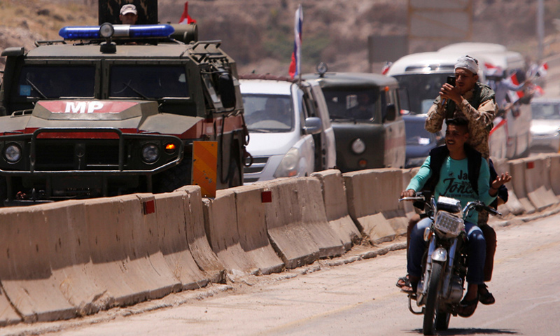 A Syrian soldier takes photos near a Russian military vehicle, in a convoy during the reopening of the road between Homs and Hama - June 2018 (Reuters)