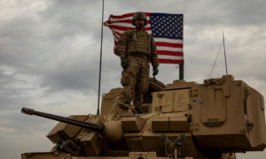 A soldier from the International Coalition Forces (ICF) standing on an armored vehicle with the American flag behind him - 24 November 2020 (International Coalition)